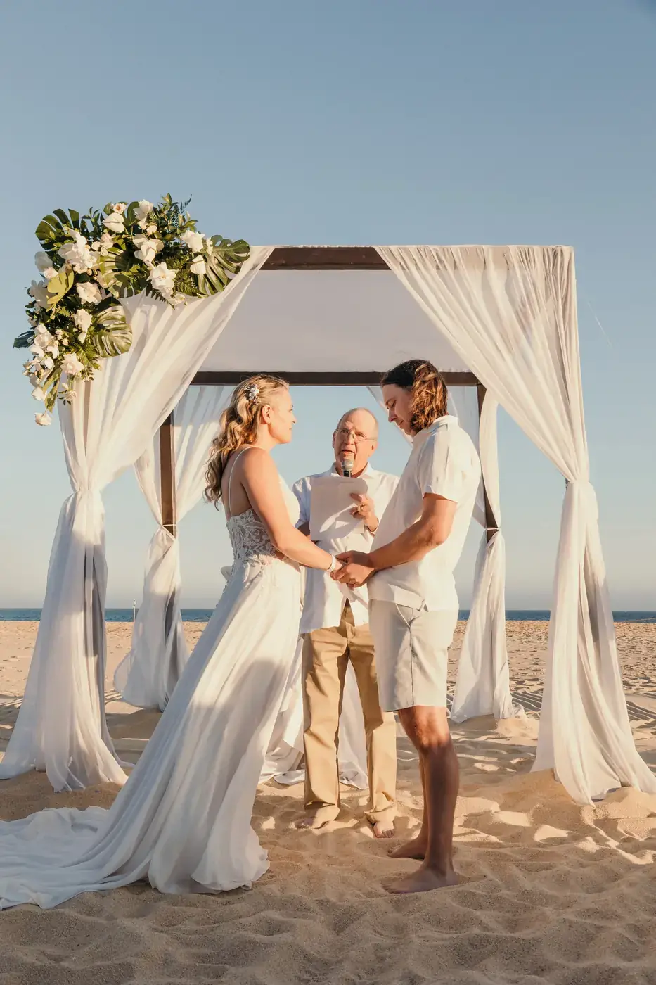 Bride and groom under a floral arch on the beach, Cabo San Lucas wedding