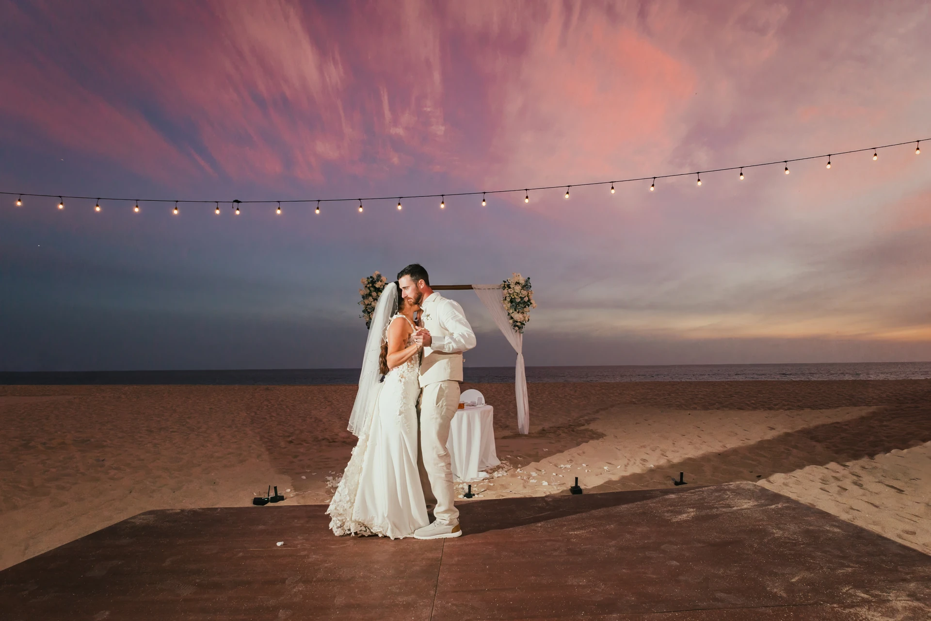 Couple under string lights at dusk on the beach, Cabo San Lucas wedding
