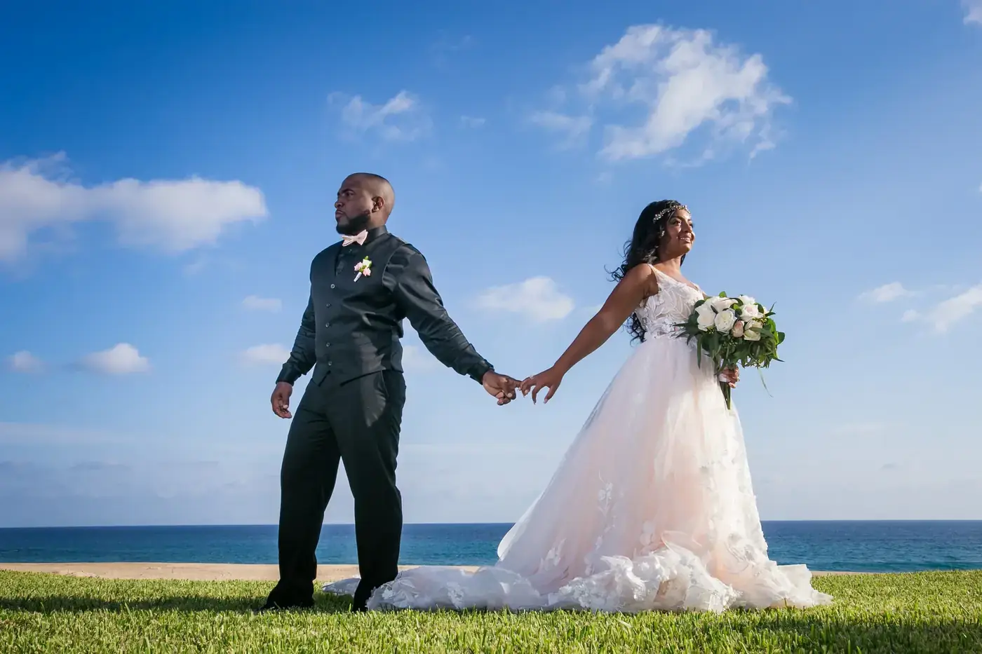 Bride and groom walking hand in hand on the lawn by the sea in Cabo