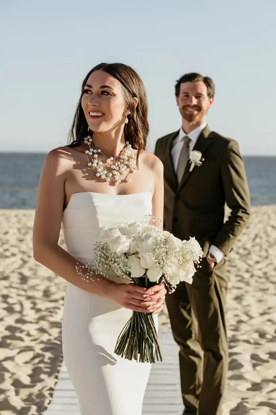 Bride with bouquet and groom behind her by the ocean in Cabo San Lucas