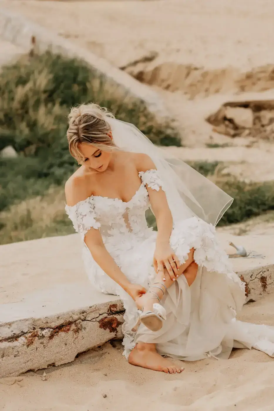 Bride adjusting her shoes on the rocks by the water in Cabo