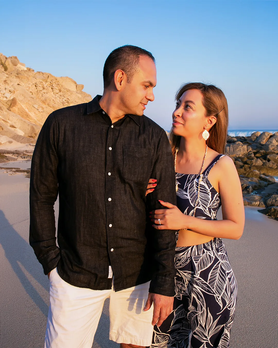 Black and white engagement photo of a couple embracing on the rocks at Playa Monumentos, Cabo San Lucas
