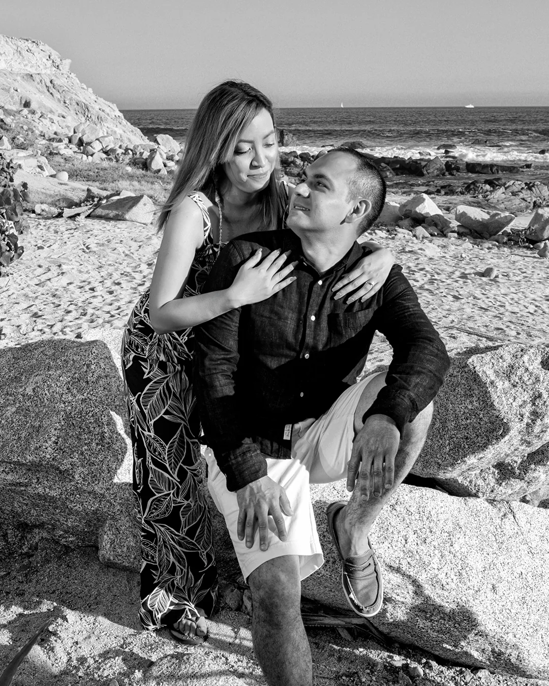Black and white couple portrait on the rocks by the sea at Monuments Beach, Cabo San Lucas