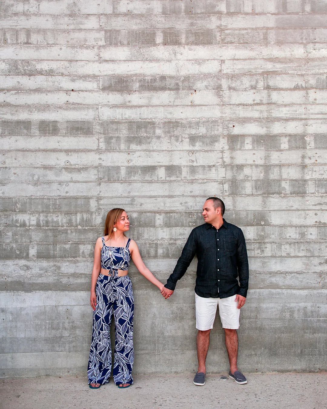 Couple holding hands against a textured stone wall near Playa Monumentos, Cabo San Lucas