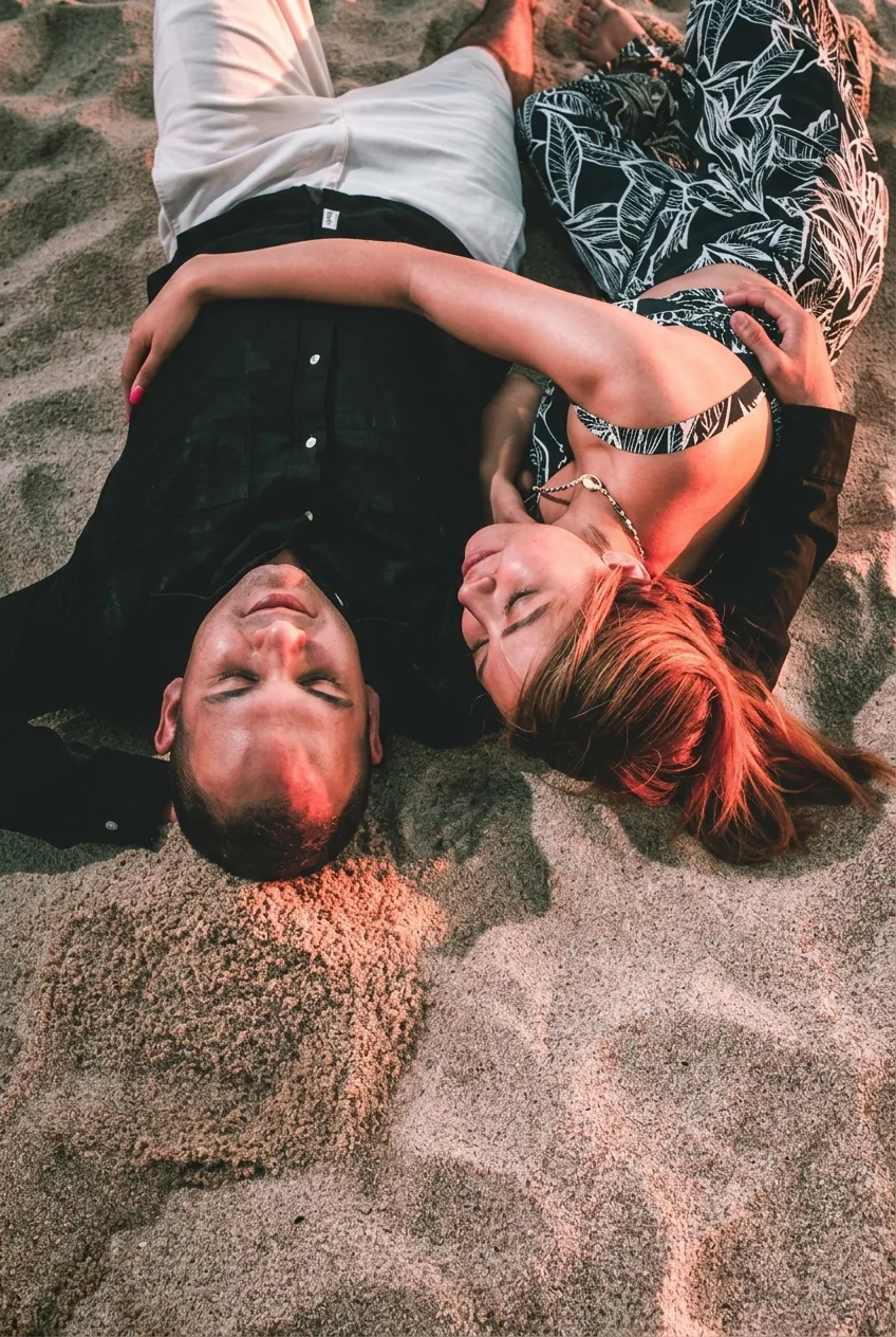 Couple lying on the sand in golden light during an engagement session at Playa Monumentos, Cabo San Lucas