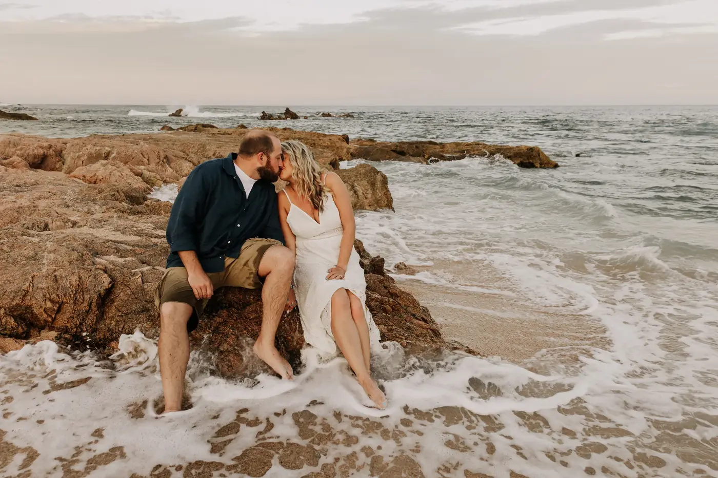 Couple sitting close on the rocks by the waves in Los Cabos