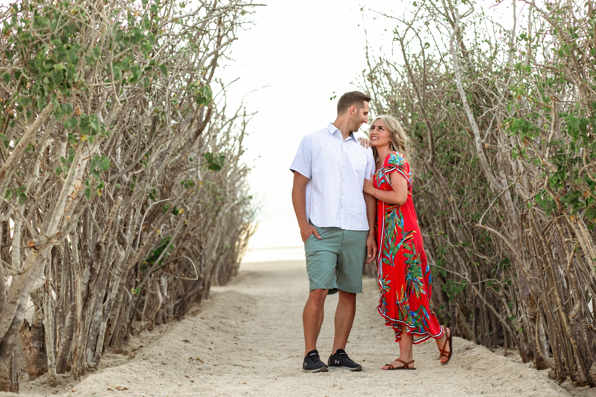 Couple walking hand in hand down the sandy tree-lined path to the beach at Playa Monumentos, Cabo San Lucas
