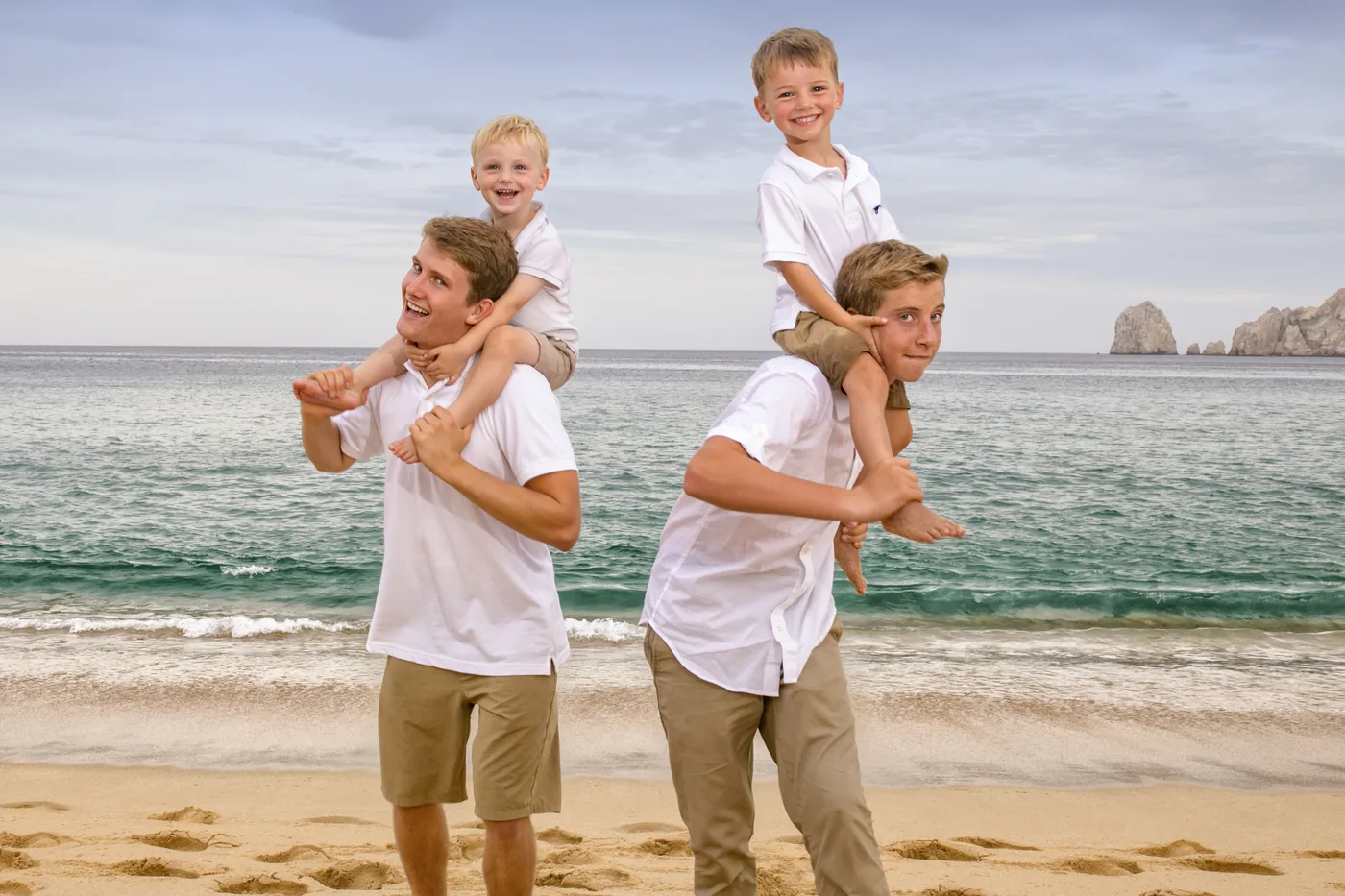 Dad carrying his kids on his shoulders during a beach session in Cabo